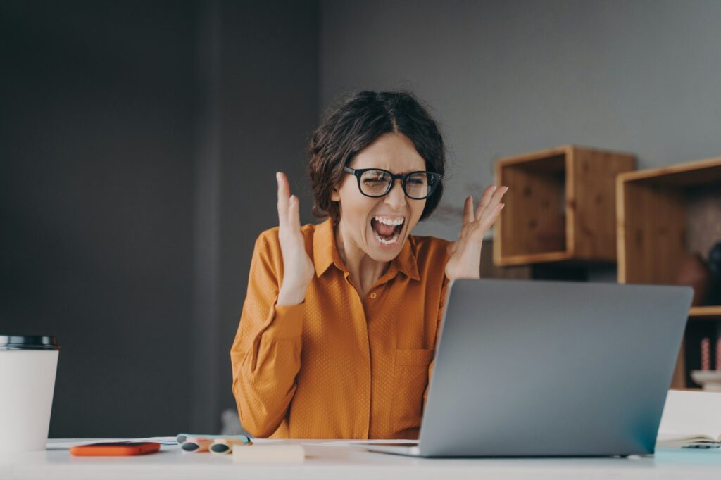 Mad Italian businesswoman shouting in distress from hopelessness while working online on laptop