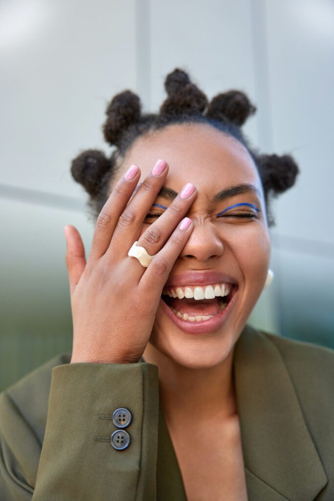 Outdoor shot of happy carefree woman smiles broadly shows white teeth makes face palm being amused b