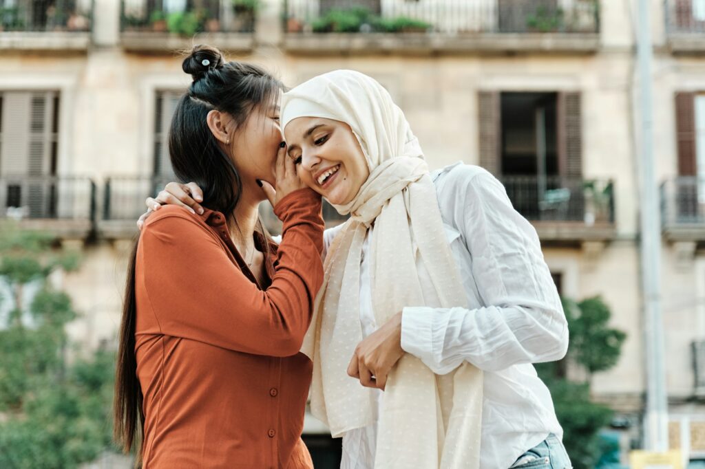 Woman whispering a secret to her friend outdoors on the street.